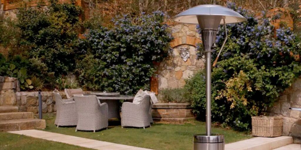 Sahara X13 patio heater stands on patio in autumnal garden with wicker garden furniture on lawn in the background