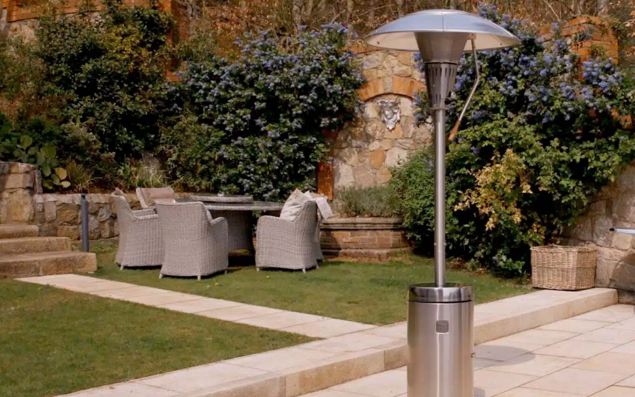Sahara X13 patio heater stands on patio in autumnal garden with wicker garden furniture on lawn in the background