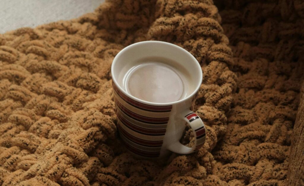 A mug of hot chocolate is on a chunky woollen blanket on a sofa